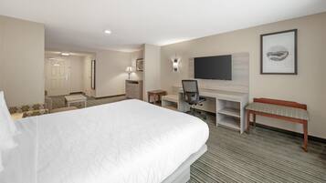 Ein Hotelzimmer mit einem großen Bett, einem Schreibtisch mit Stuhl, einem an der Wand befestigten Fernseher, einer Bank und einer Tür zu einem weiteren Raum.