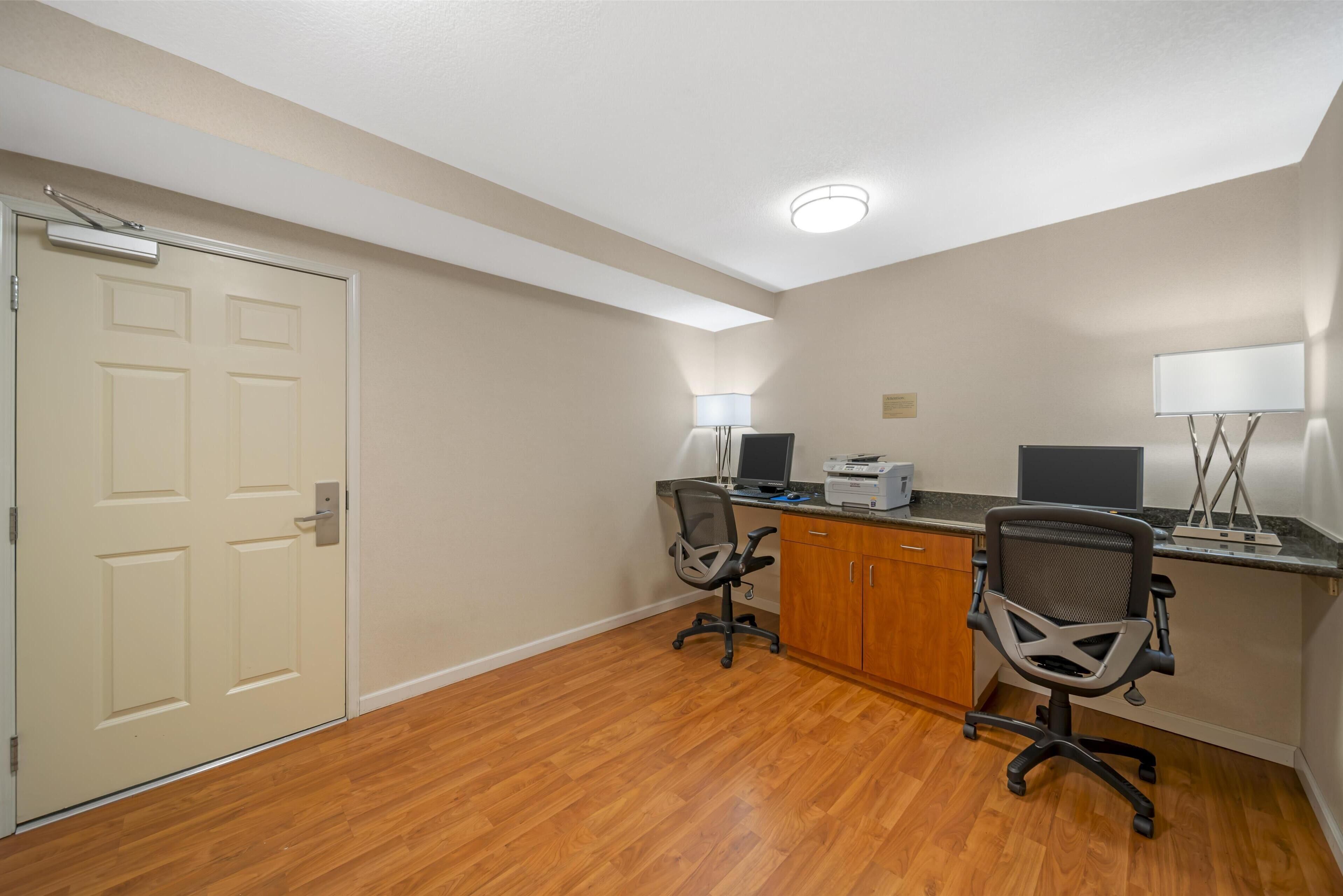 A small office with two desks, chairs, a printer, and a door.