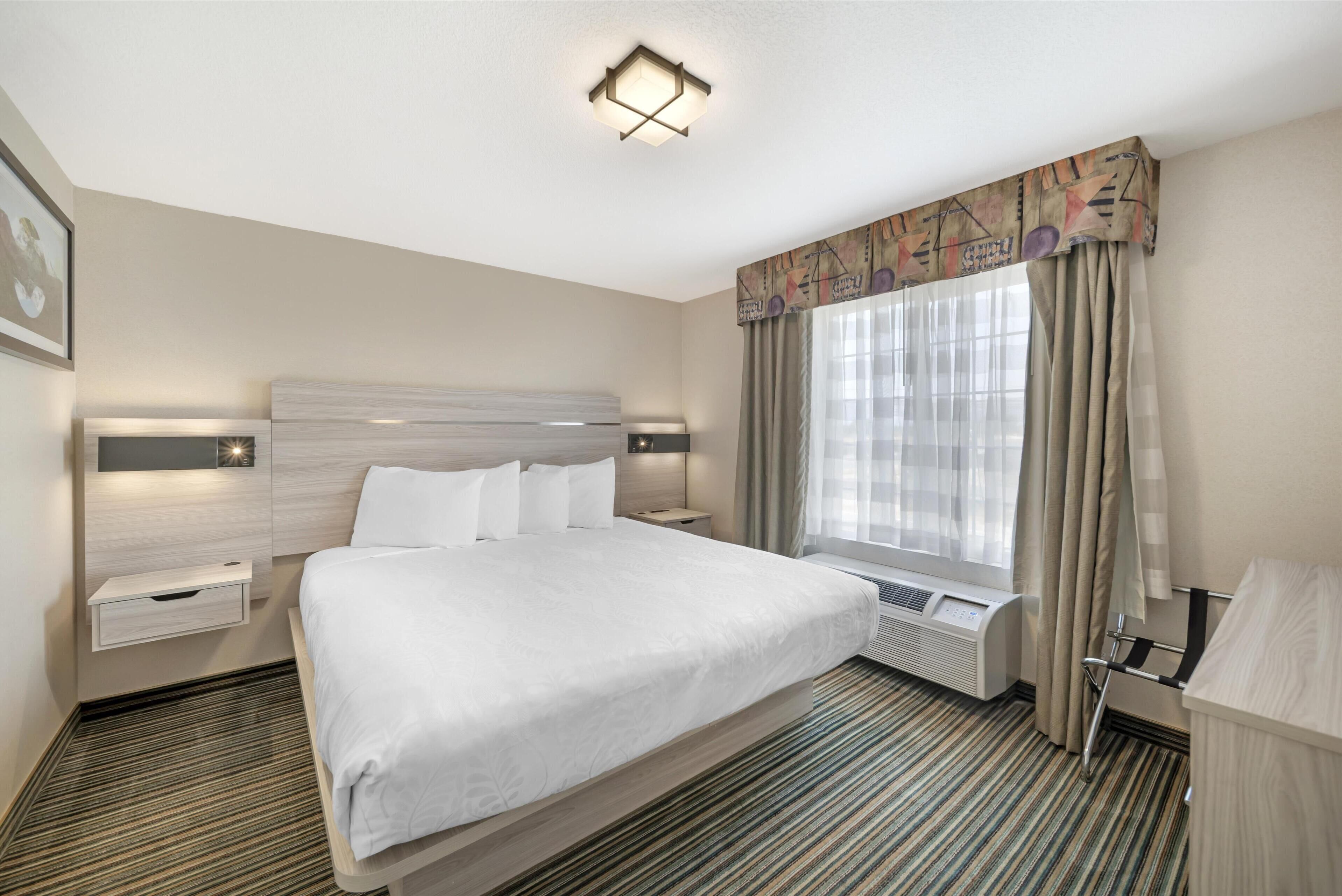 A hotel room with a large bed, bedside tables, a desk, and a window with curtains.