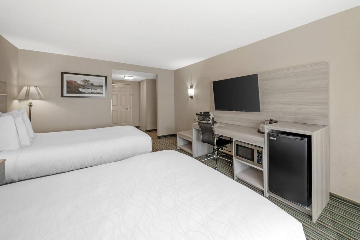 A hotel room with two beds, a desk with a computer, a television, and a refrigerator.