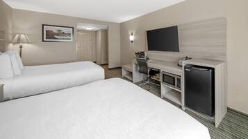 A hotel room with two beds, a desk with a computer, a television, and a refrigerator.