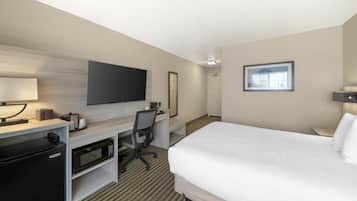 Una camera d'albergo con un letto, una scrivania con un computer, un forno a microonde, un frigorifero, una televisione e un quadro appeso al muro.