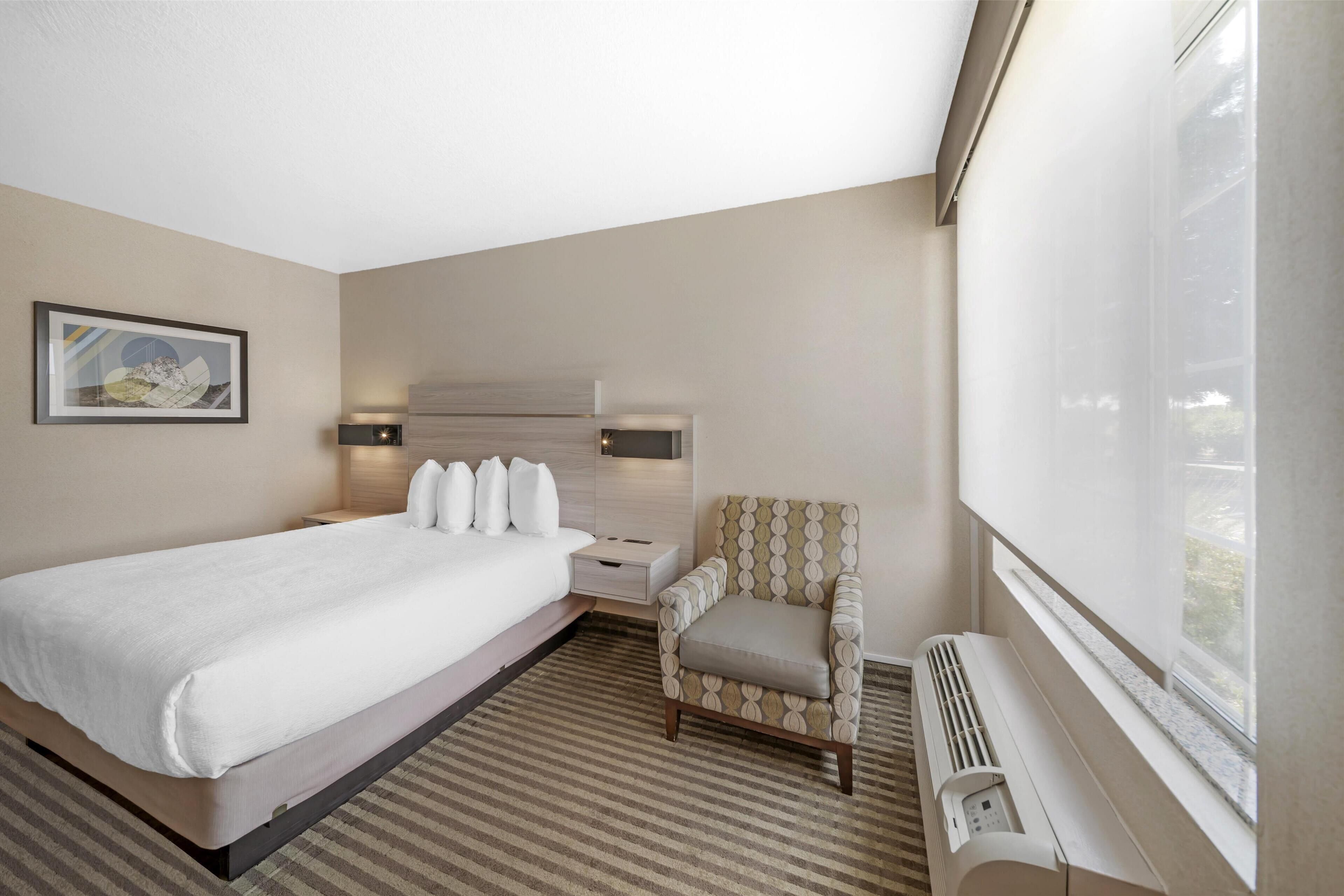 Hotelkamer met een groot bed, een stoel, een nachtkastje, een wandheater en een raam met uitzicht.