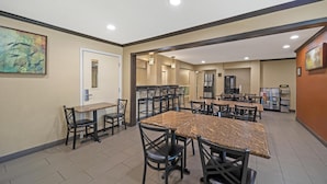 A spacious dining area with multiple tables and chairs, a kitchen area with stainless steel appliances, and a door leading to another room. - Best Western Plus Twin View Inn & Suites (Redding)