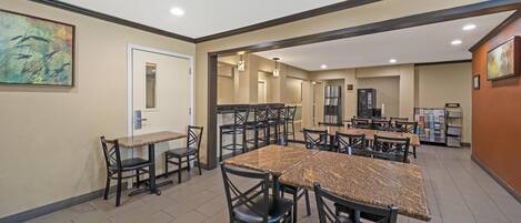 A spacious dining area with multiple tables and chairs, a kitchen area with stainless steel appliances, and a door leading to another room.