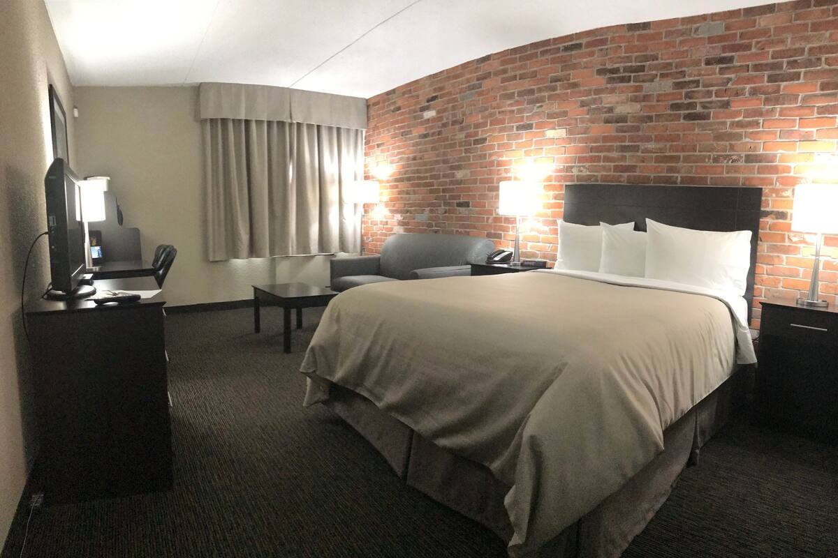 Hotellihuone, jossa on tiiliseinä, suuri sänky, työpöytä tuolilla ja kaksi yöpöytävalaisinta.