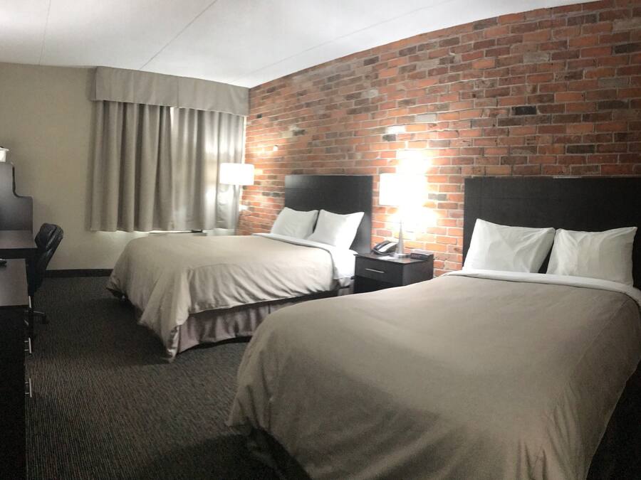 Ein Hotelzimmer mit zwei Betten, einem Schreibtisch mit Computer, einem Stuhl und einer Backsteinwand.