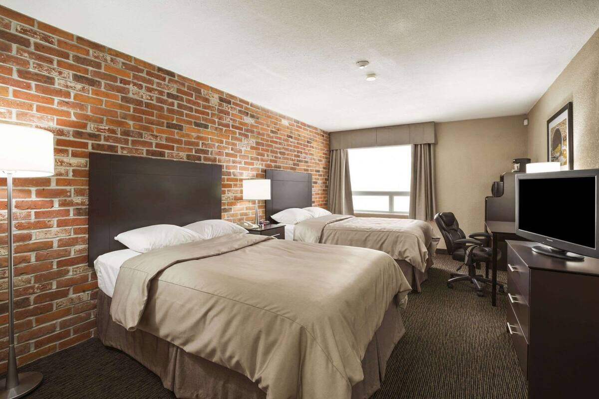 Hotellihuone, jossa on kaksi sänkyä, televisio, työpöytä ja tiiliseinä.