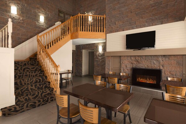 Un restaurant doté d’une cheminée en pierre, d’un escalier en bois et d’un téléviseur à écran plat fixé au mur.