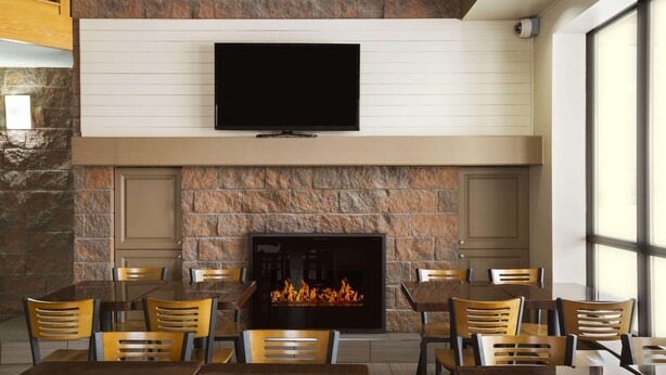 Een restaurant met een stenen openhaard, houten stoelen en een flatscreen televisie die boven de openhaard hangt.