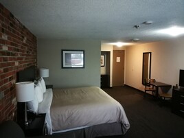 Una habitación de hotel con cama, escritorio, silla, televisor y lámpara.