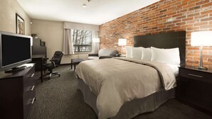 Een hotelkamer met een bakstenen muur, een groot bed, een bureau met een televisie en een stoel.
