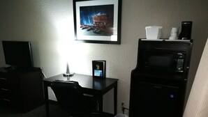 Een hotelkamer met een bureau, stoel, een inlijsting foto aan de muur, een magnetron en een prullenbak.