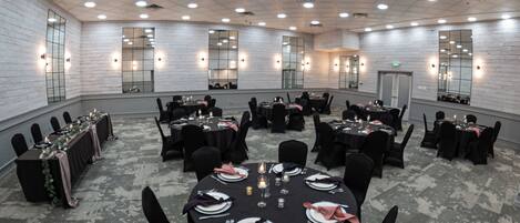 Un salón de conferencias con varias mesas, sillas negras y paredes blancas con espejos.