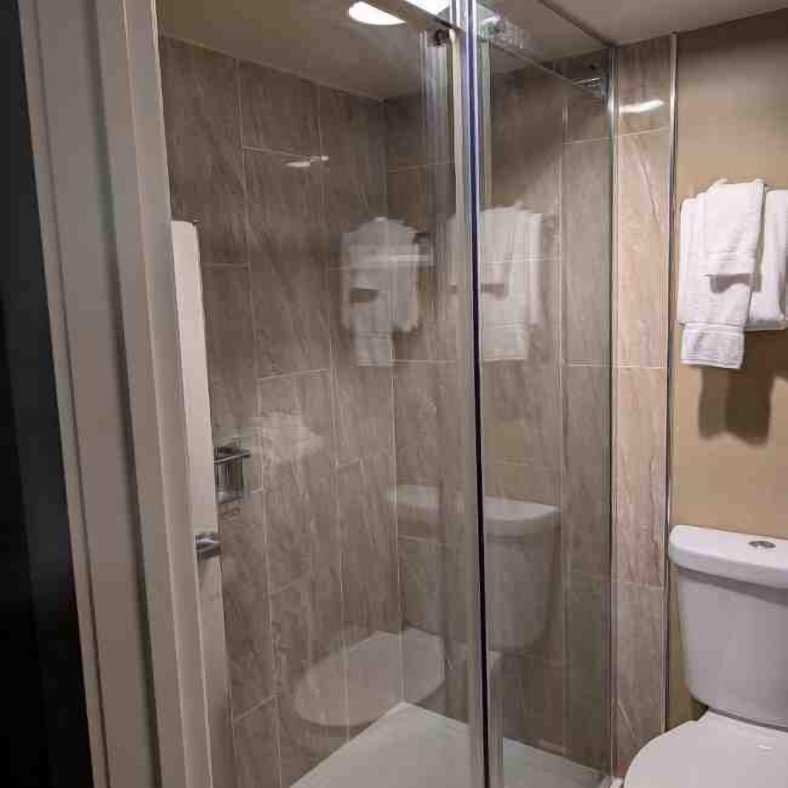 Un baño con ducha de vidrio, inodoro y perchero para toallas.