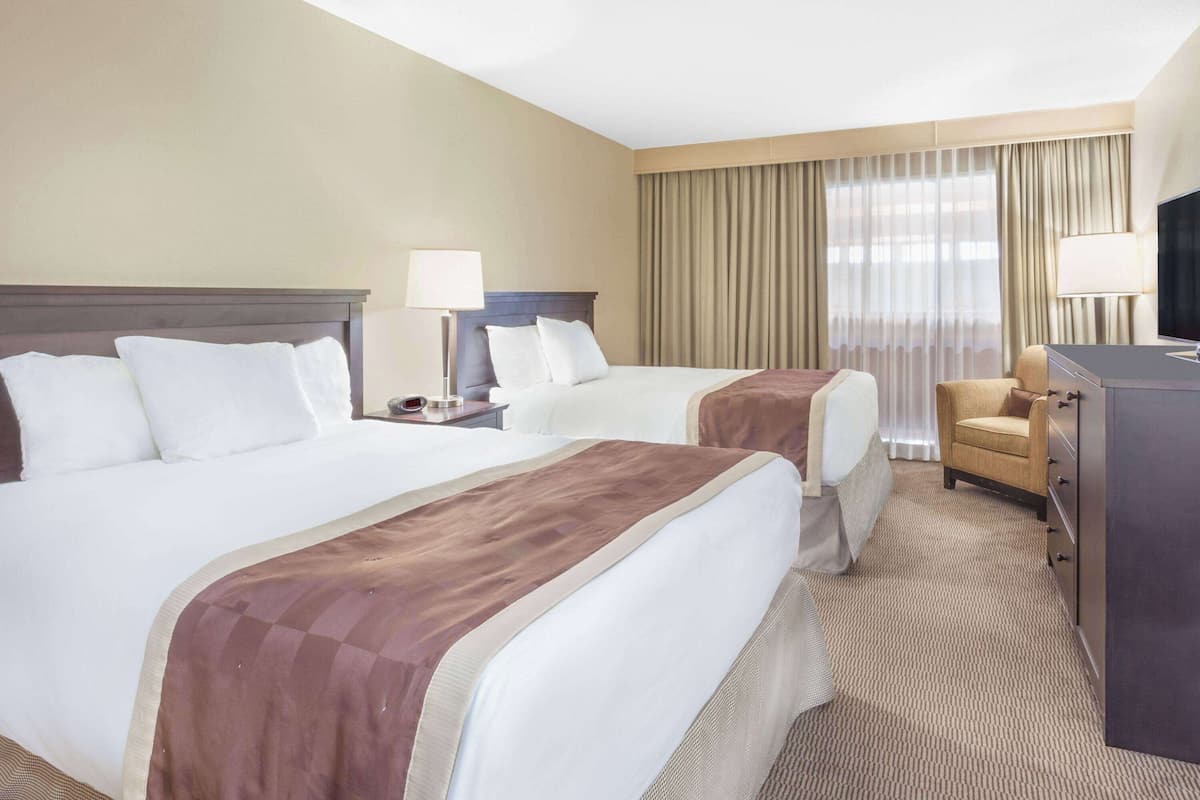 Ein Hotelzimmer mit zwei Betten, einem Schreibtisch, einem Stuhl und einem Fernseher.