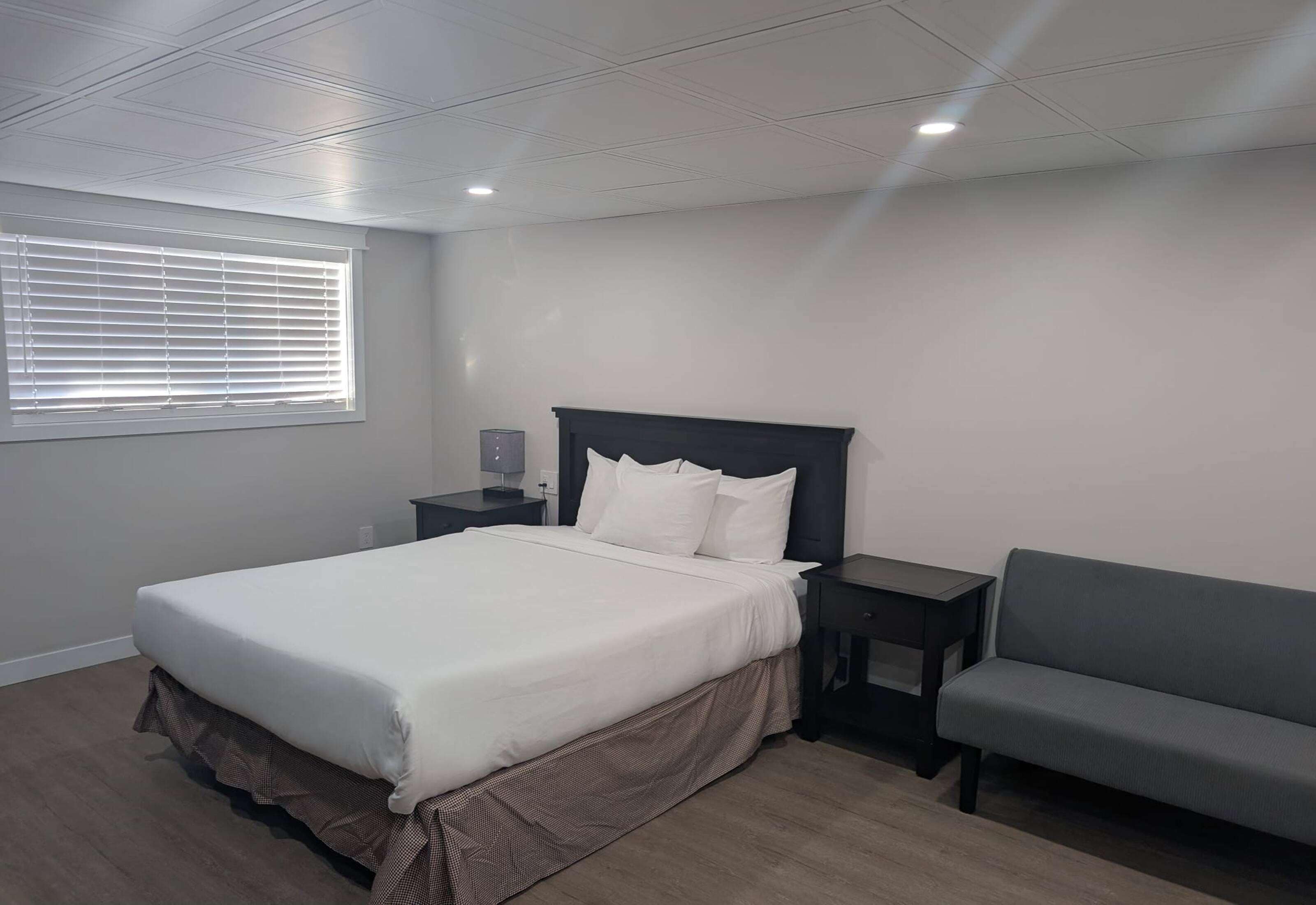 A bedroom with a bed, a nightstand, a lamp, a sofa, and a window with blinds.