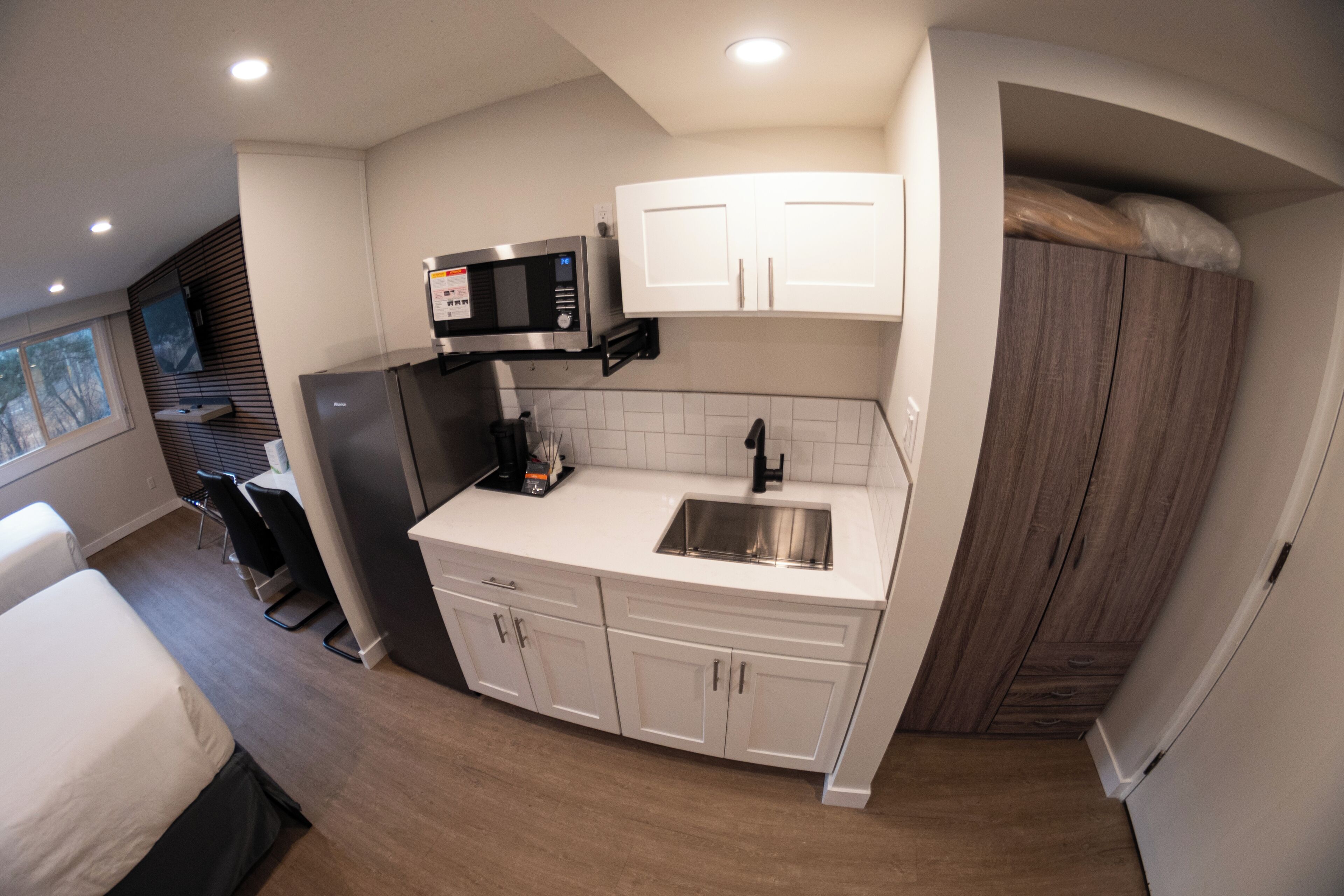 A compact kitchen with a microwave, sink, and white cabinets.
