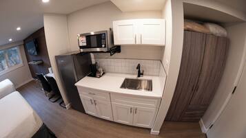 A compact kitchen with a microwave, sink, and white cabinets.