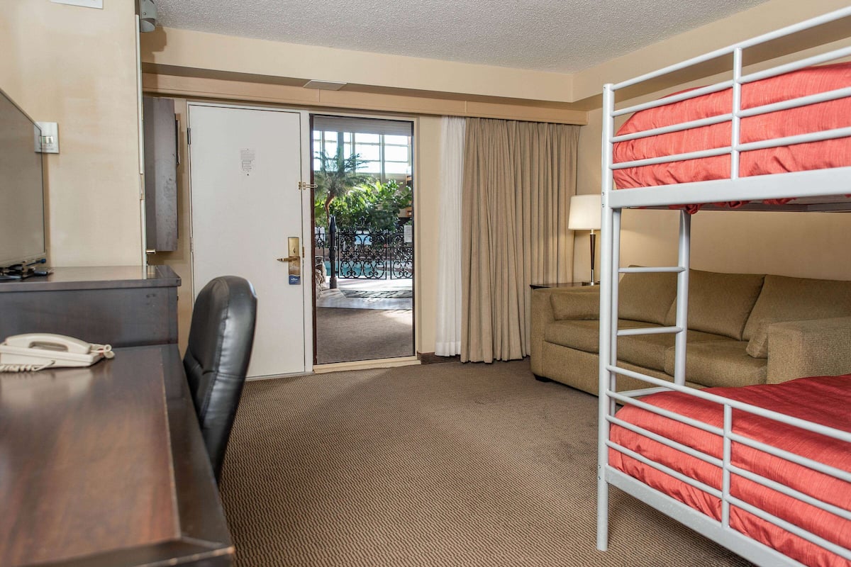 Ein Hotelzimmer mit Etagenbett, Schreibtisch mit Telefon, Stuhl und Blick durch eine Tür nach draußen.