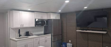 Una cocina moderna con armarios blancos, un refrigerador de acero inoxidable, un microondas y un televisor integrado.