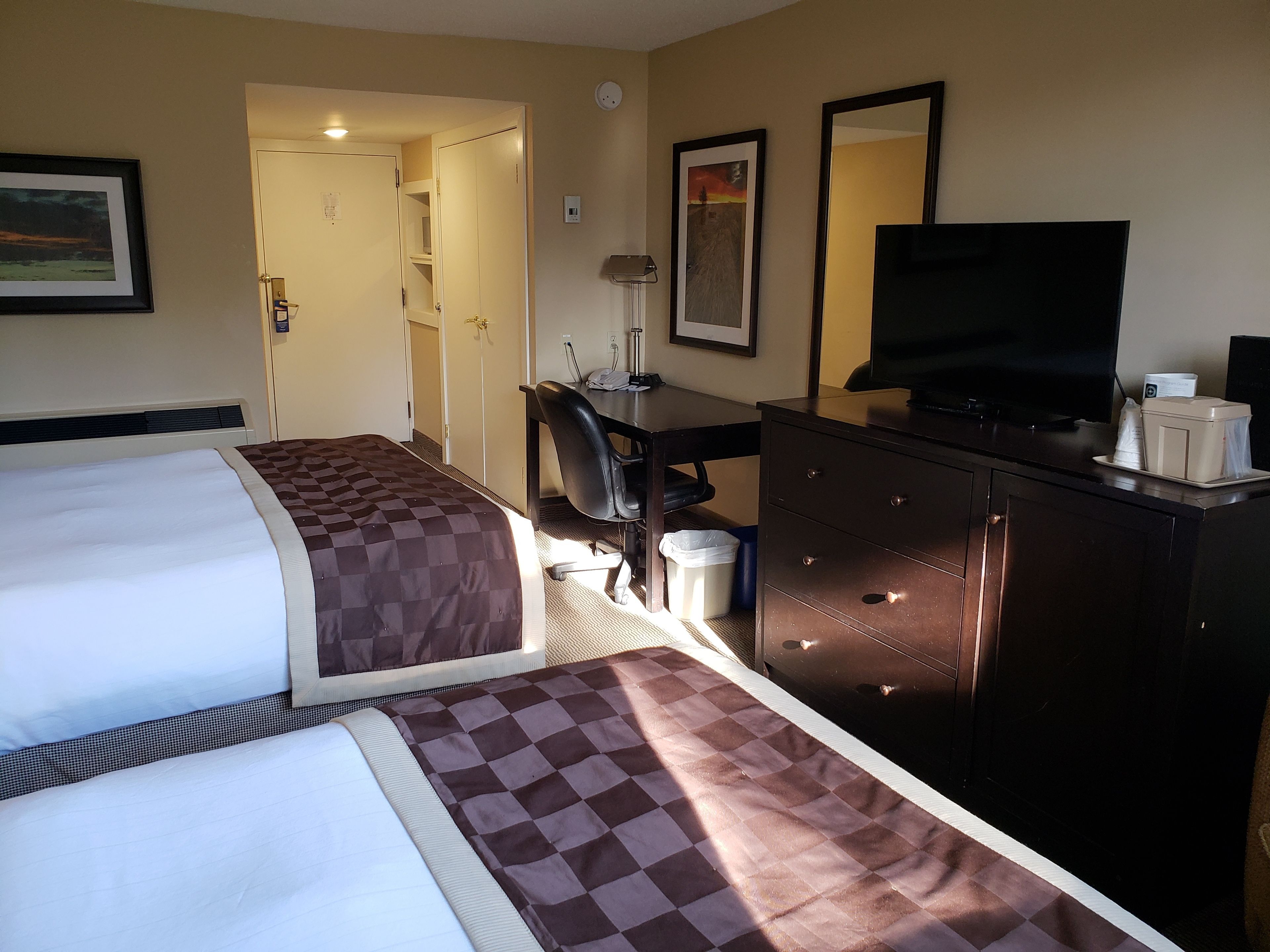 Een hotelkamer met twee bedden, een bureau, een televisie en een dressoir.
