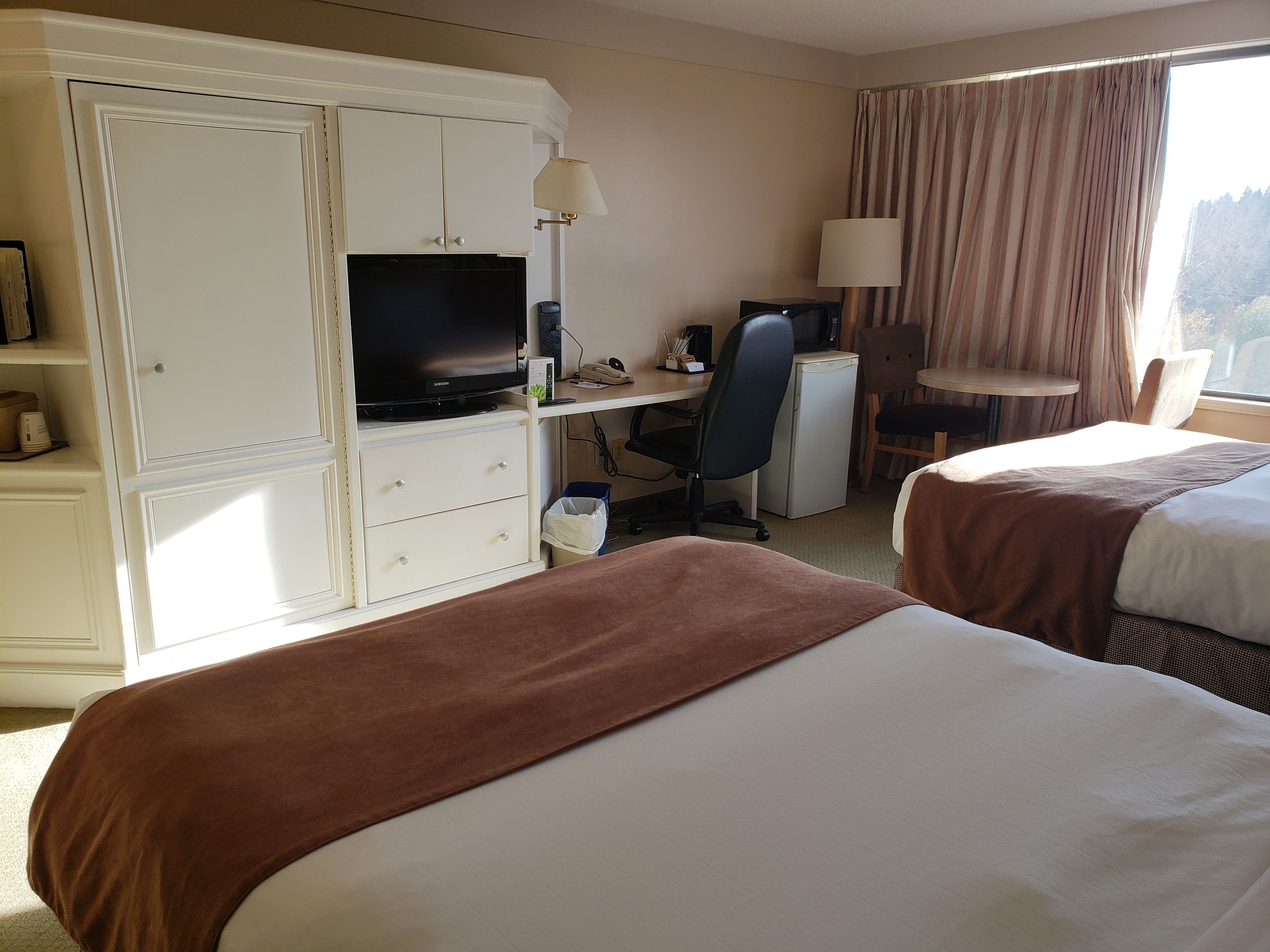 Une chambre d’hôtel avec deux lits, un bureau avec un ordinateur, une télévision et un petit réfrigérateur.
