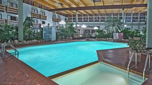 An indoor swimming pool with tiled edges, surrounded by plants and a wooden deck. - Baymont by Wyndham Red Deer (Red Deer)