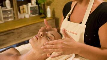 A person receiving a facial treatment in a spa setting with shelves of products in the background.