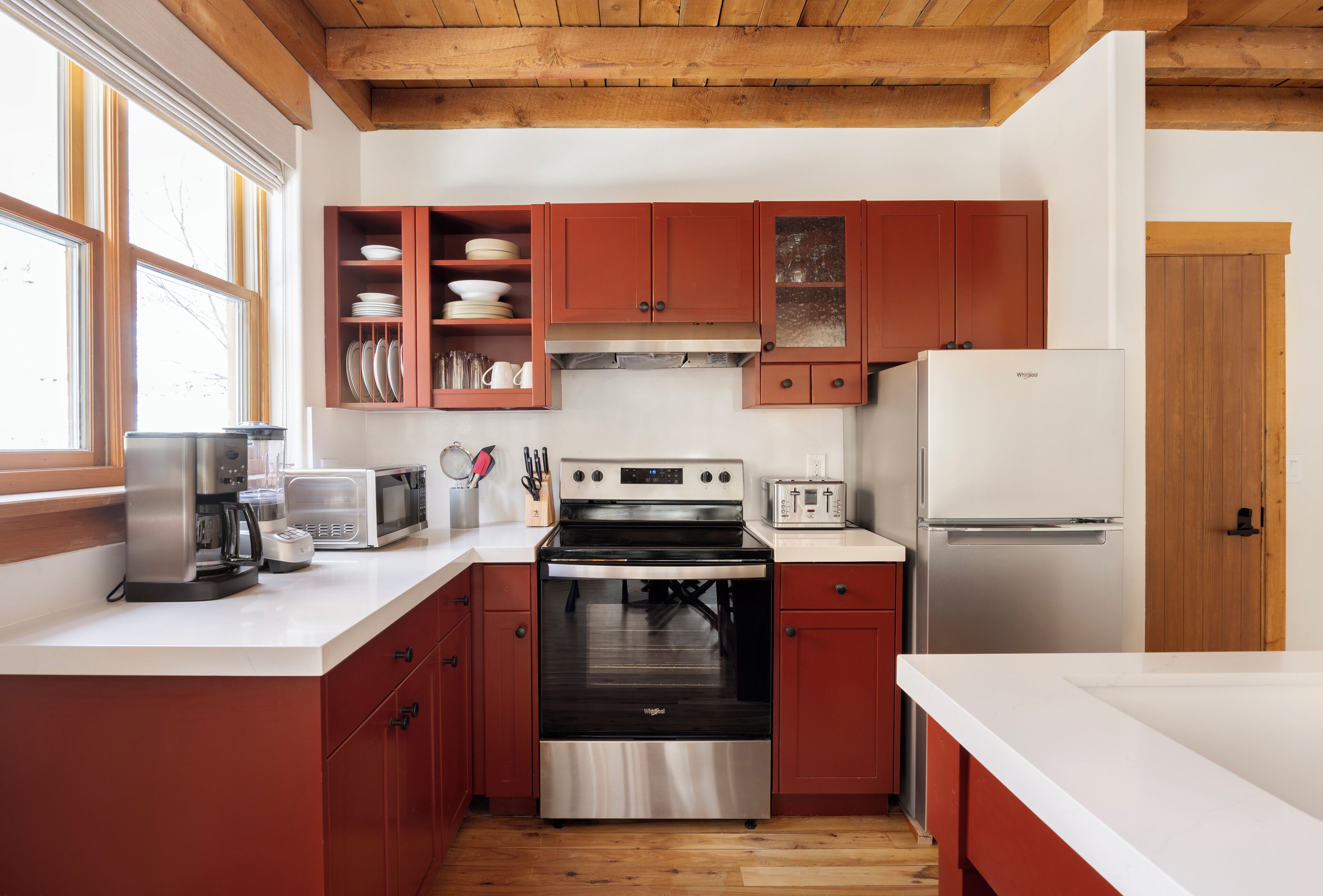 A modern kitchen with stainless steel appliances, red cabinetry, and a white countertop.