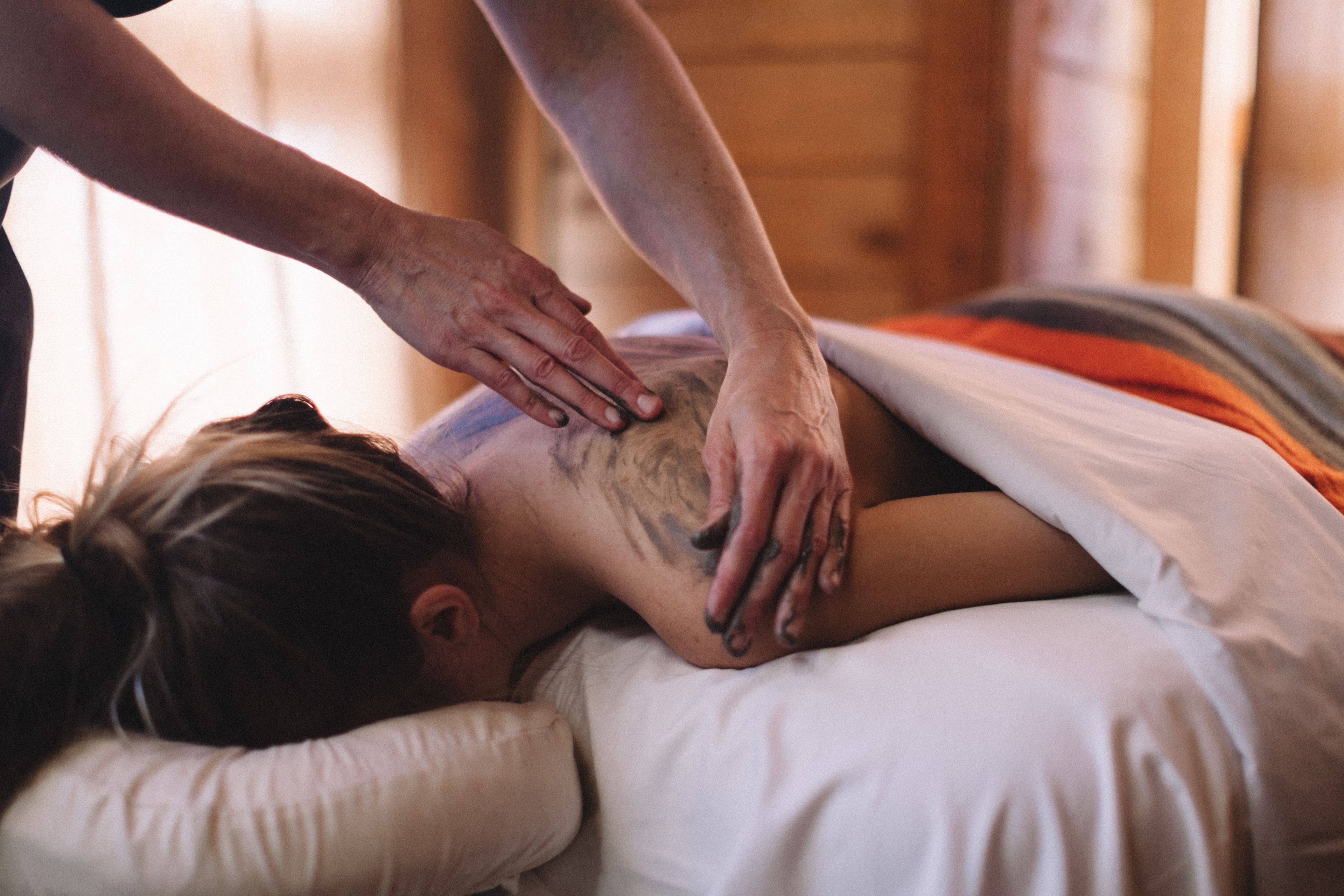 A person receiving a massage on a bed in a room with wooden walls.