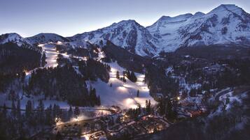 A snow-covered mountain resort at dusk with illuminated ski slopes and a small town below.
