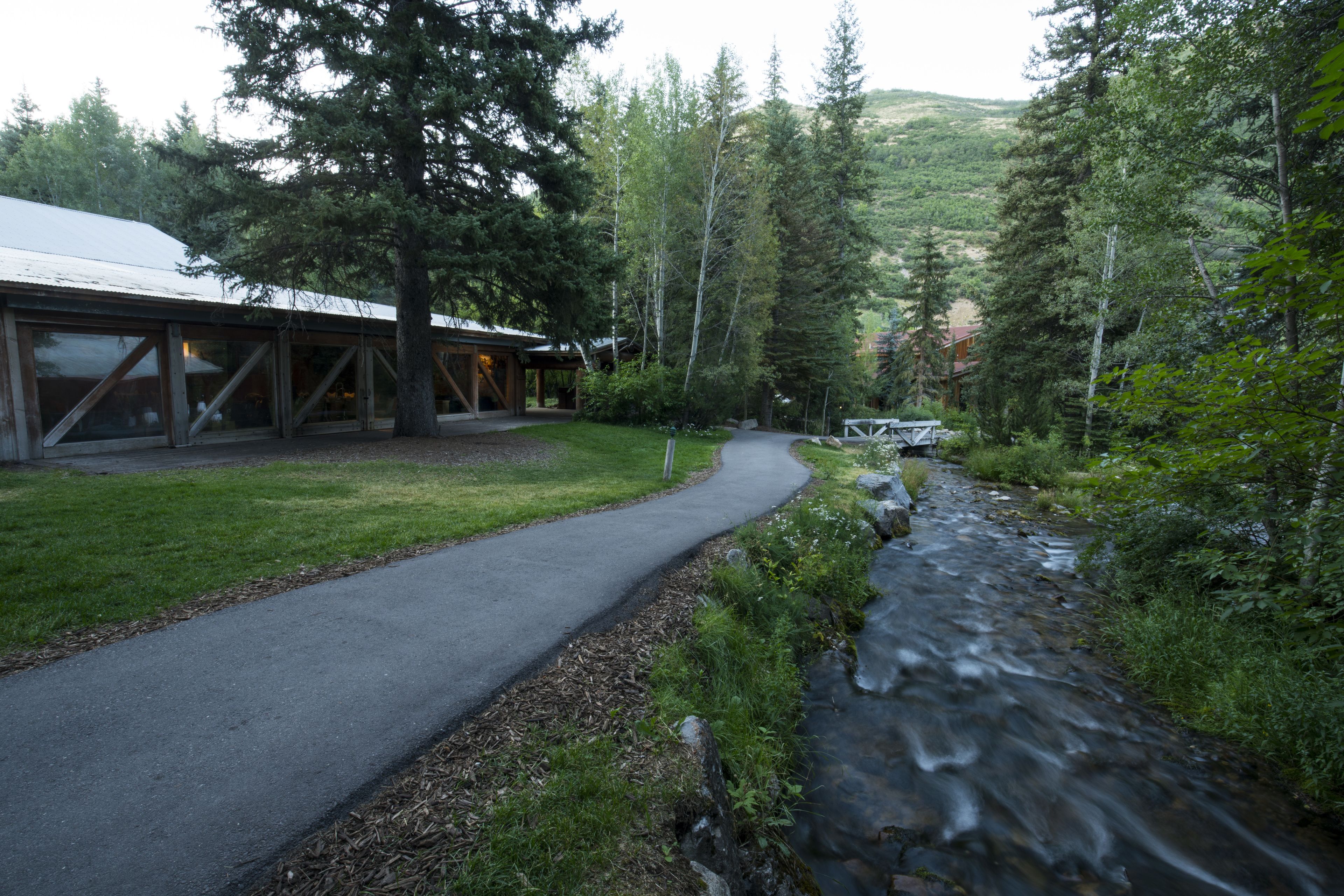 A building with a covered outdoor area, a paved path, and a stream.