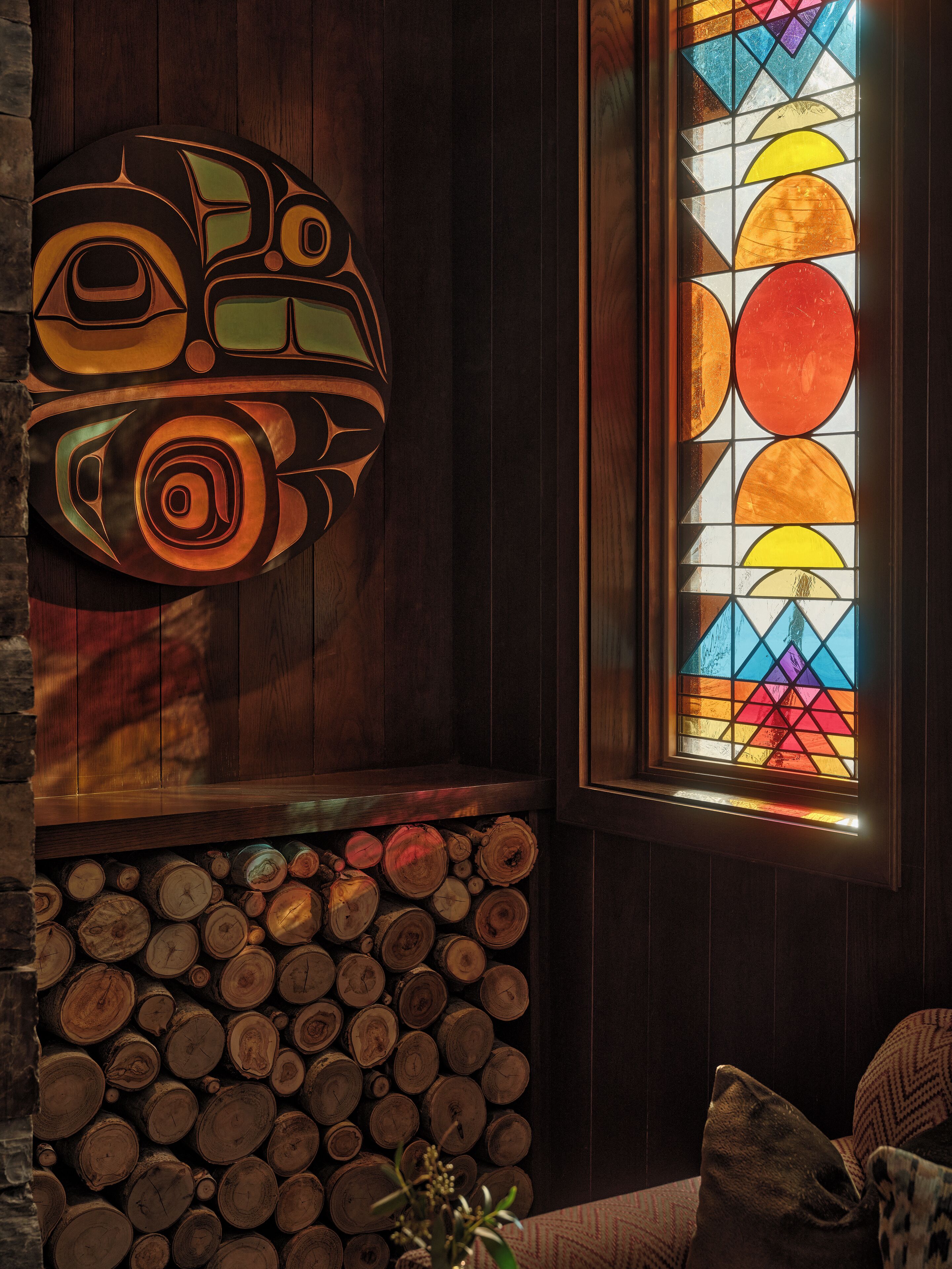 A room with a wooden wall, a colorful stained glass window, and a stack of logs.