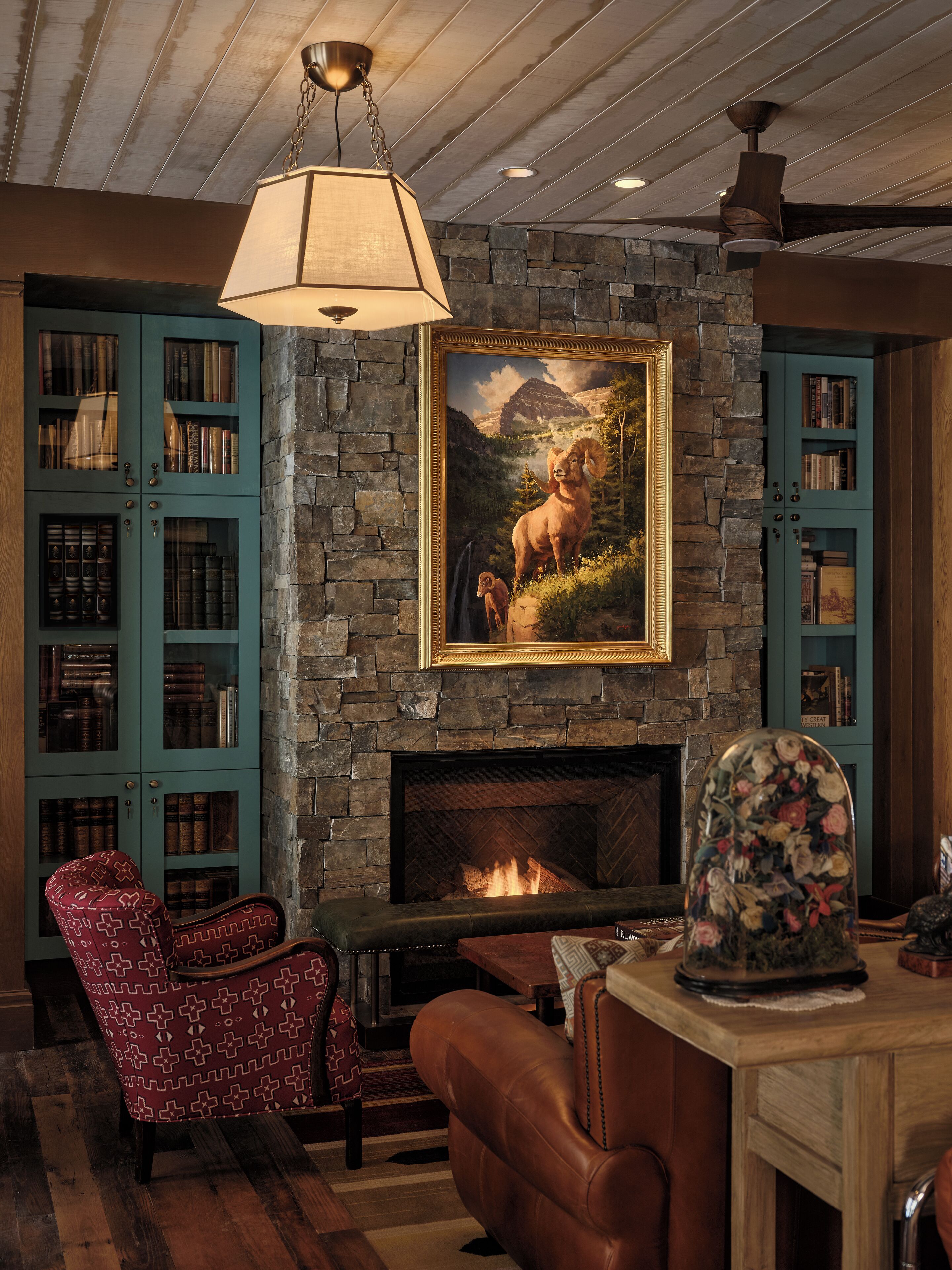 A cozy living room with a stone fireplace, bookshelves, and a mounted painting.