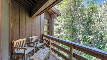 A wooden deck with two wooden chairs and a table, overlooking a forested area.