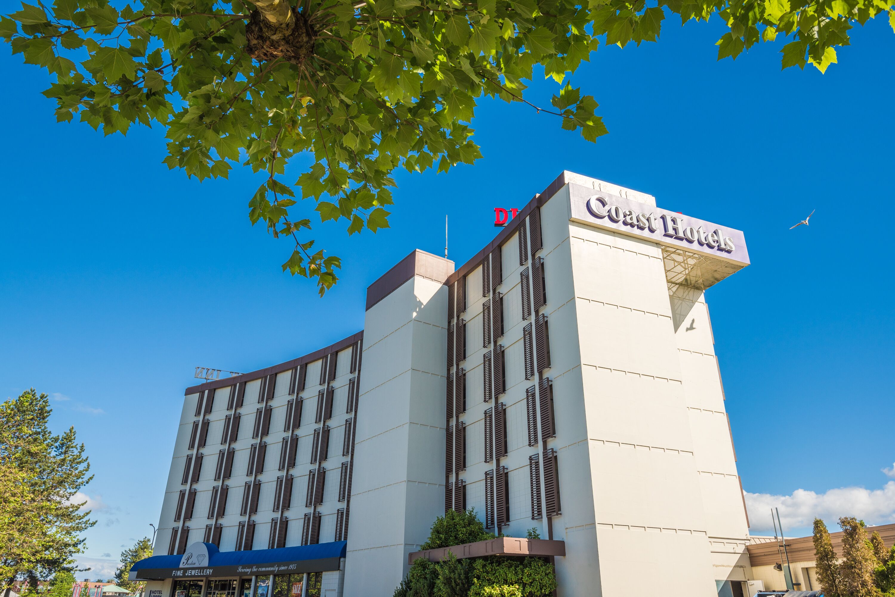 A hotel with a prominent 'Coast Hotels' sign, a 'Fine Jewellery' store on the ground floor, and a clear blue sky.