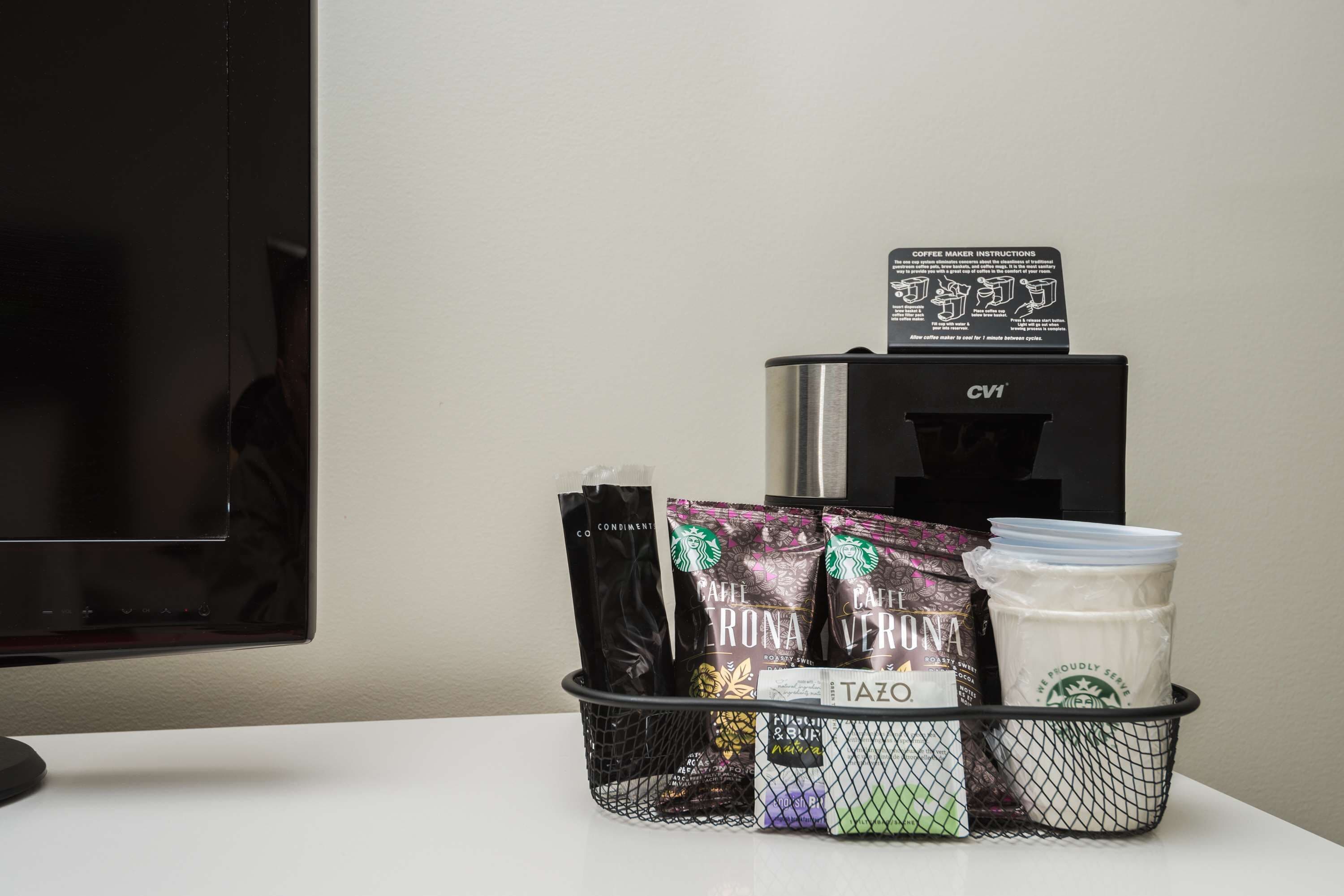 Een koffiezetapparaat met instructies, een mand met Starbucks en Tazo koffiekapsules, en een melkkruik op een tafel.