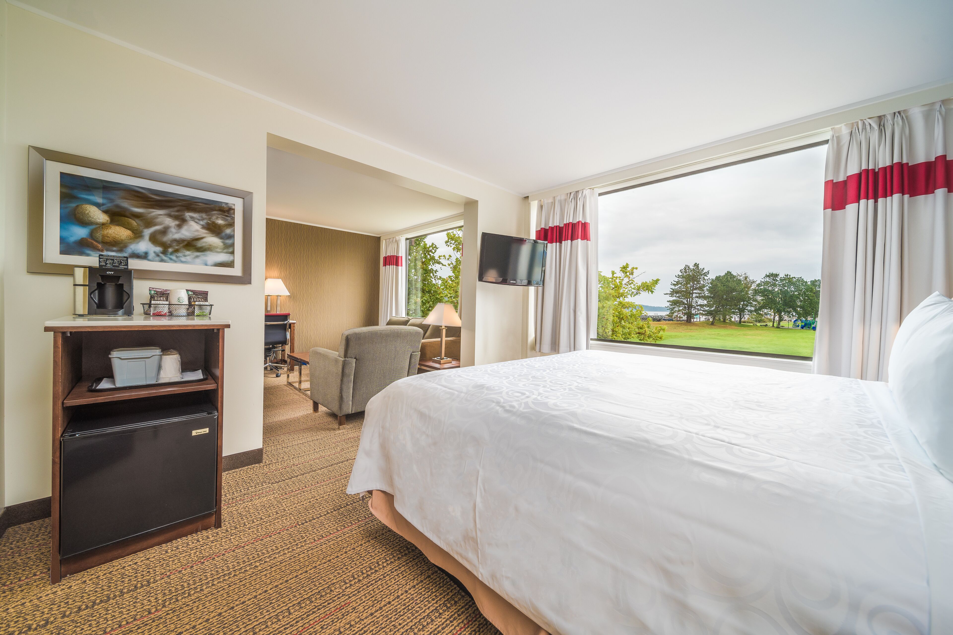 Habitación de hotel con una cama grande, televisión, escritorio con cafetera y vista al exterior.