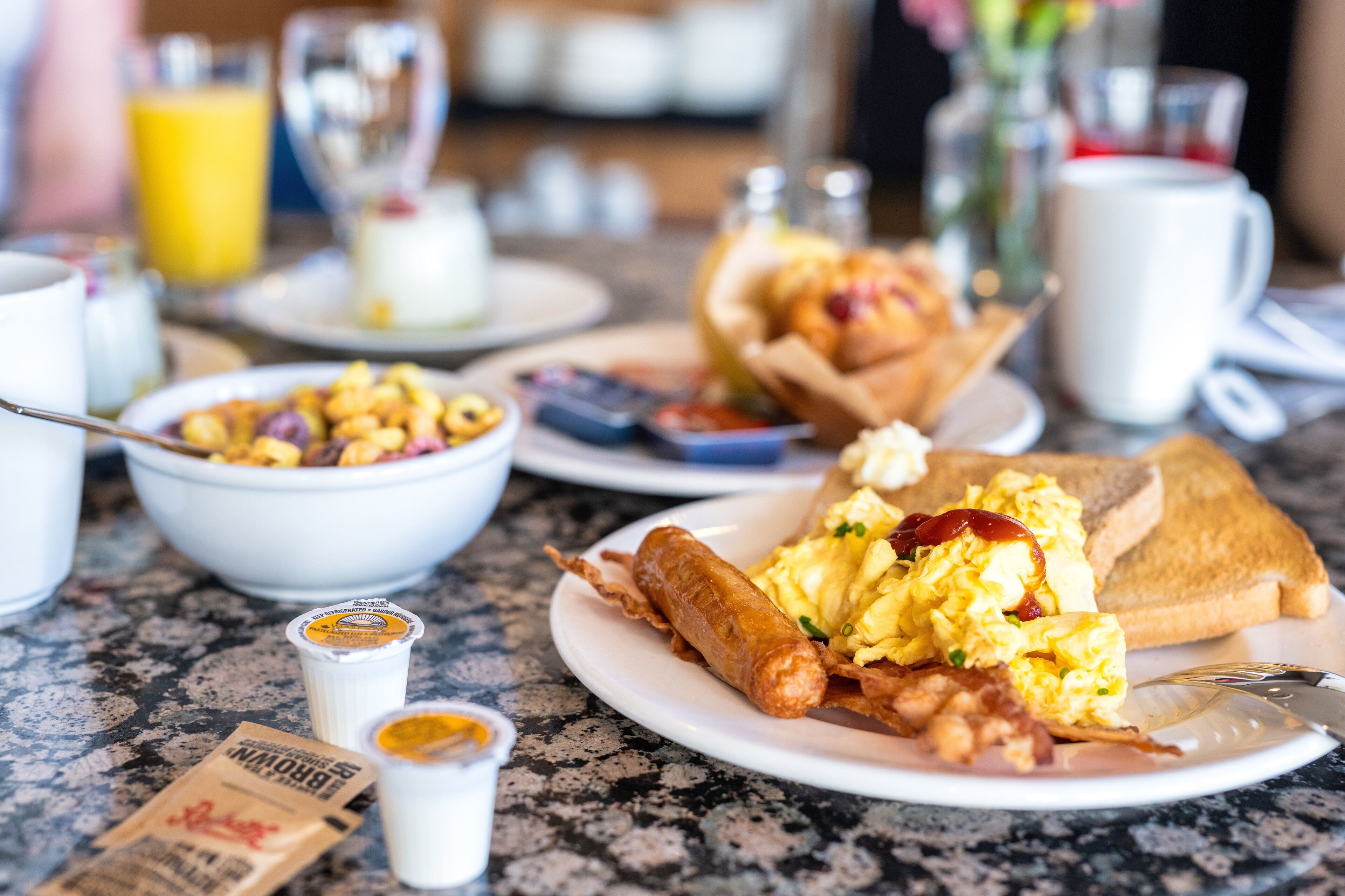 A breakfast table with various dishes including scrambled eggs, sausage, toast, and a bowl of cereal.