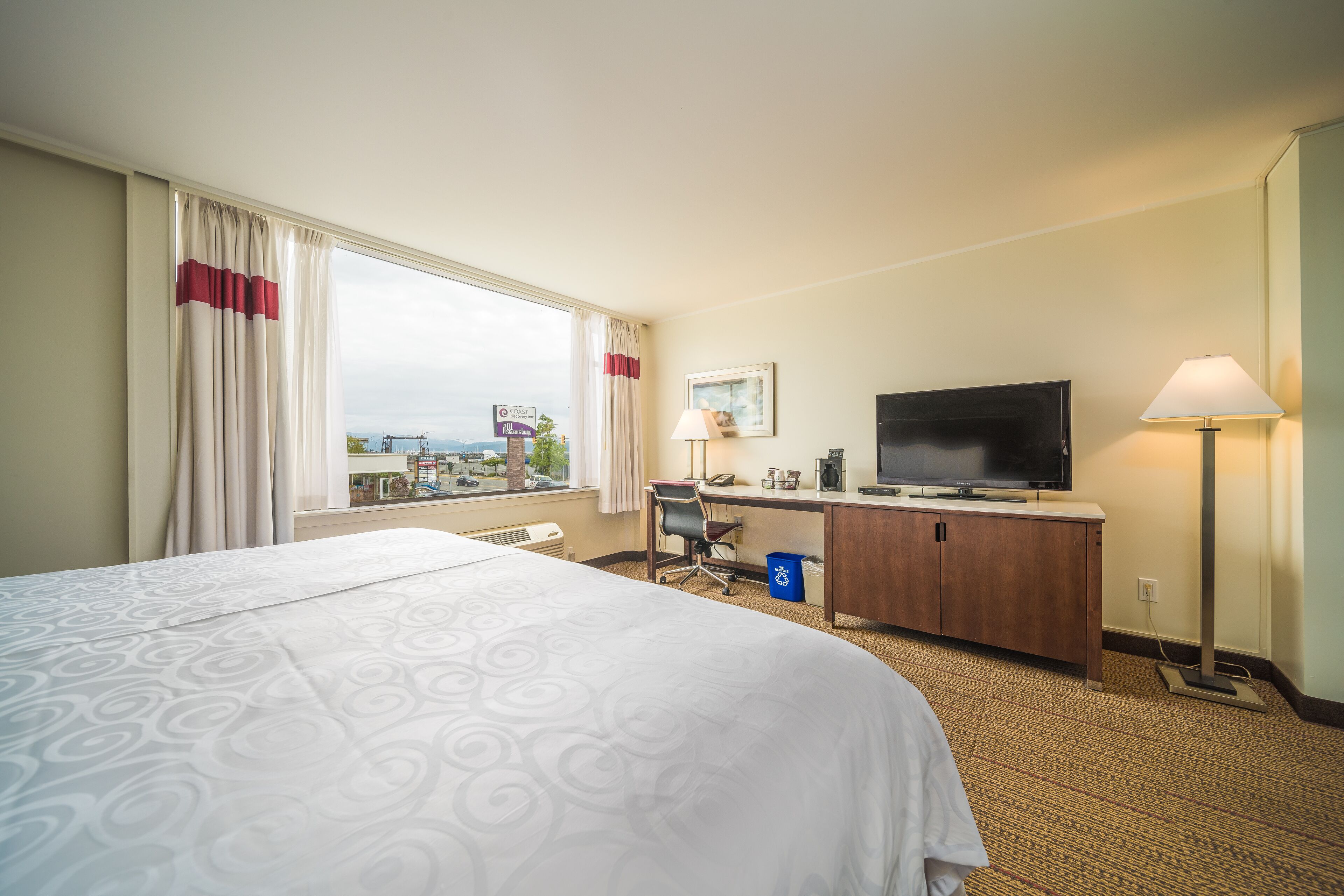 Una habitación de hotel con una cama grande, un escritorio con computadora, televisor y ventana con cortinas.