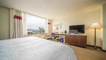 Una habitación de hotel con una cama grande, un escritorio con computadora, televisor y ventana con cortinas.
