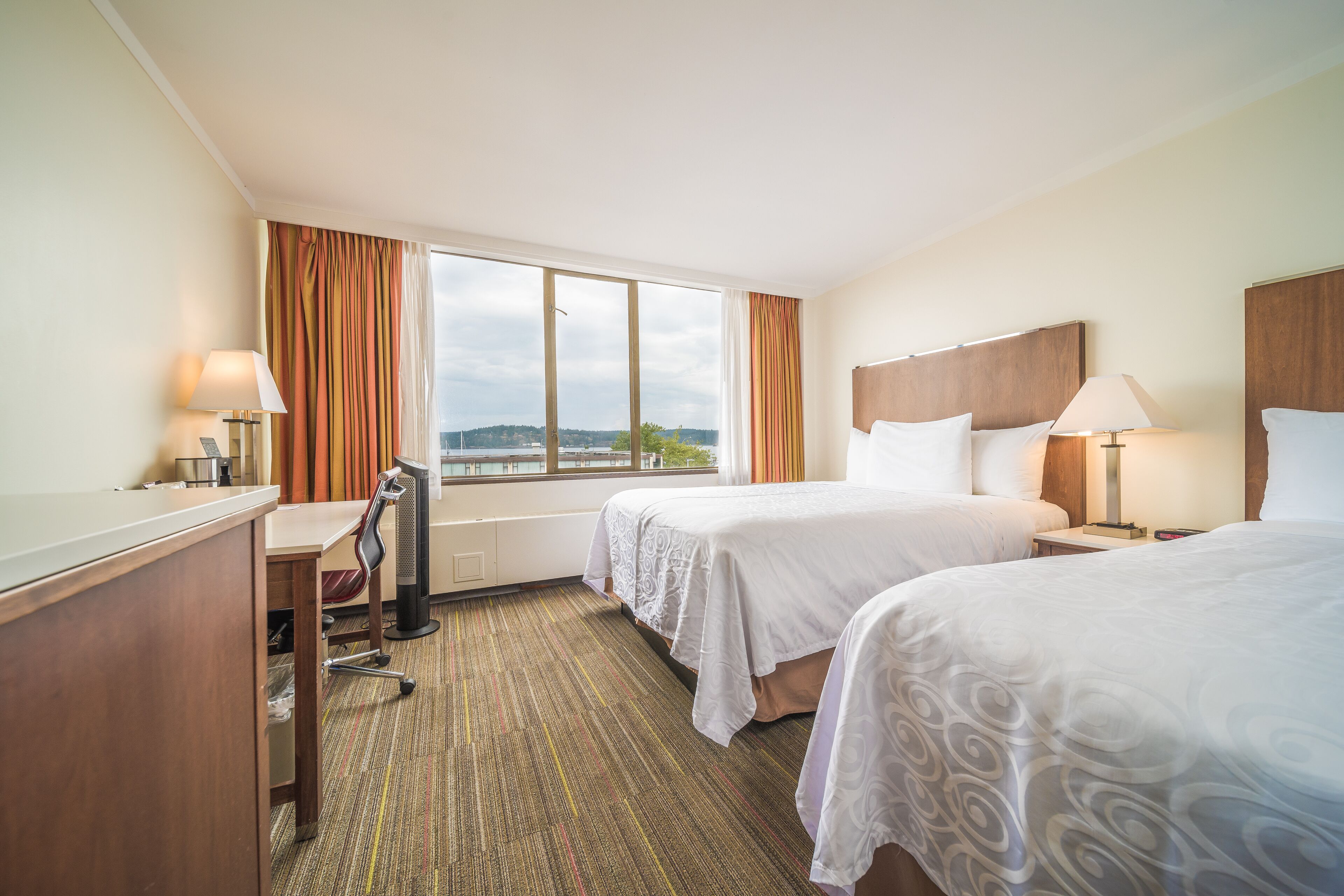 A hotel room with two beds, a desk, and a chair.