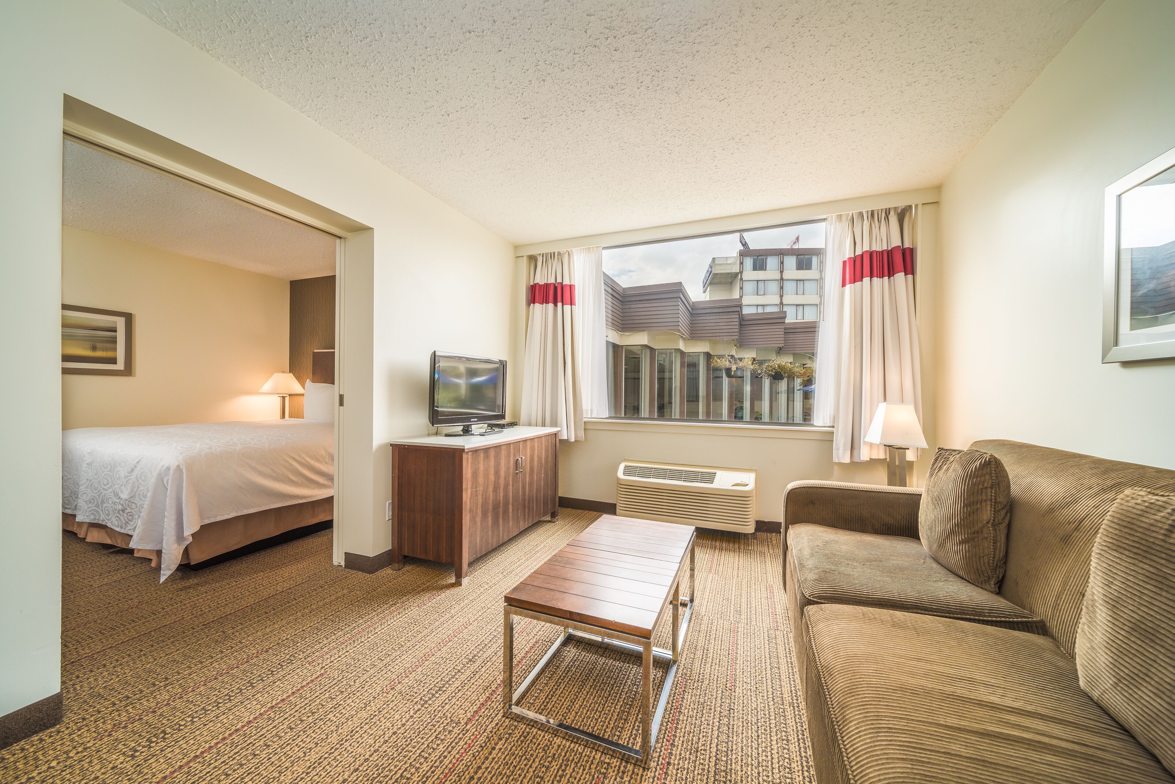 A hotel room with a bed, a TV, a desk, a sofa, and a window with curtains.