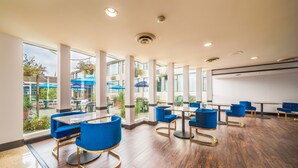 Un vaste espace intérieur doté d’un plancher en bois, de chaises et de tables bleues, ainsi que de grandes fenêtres offrant une vue sur l’extérieur.