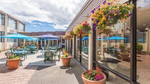 Un espace extérieur aménagé en terrasse, avec des tables et des chaises, de grandes fenêtres et des jardinières suspendues.