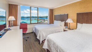 Une chambre d’hôtel avec deux lits, un bureau et une grande fenêtre donnant sur un lac et des montagnes.