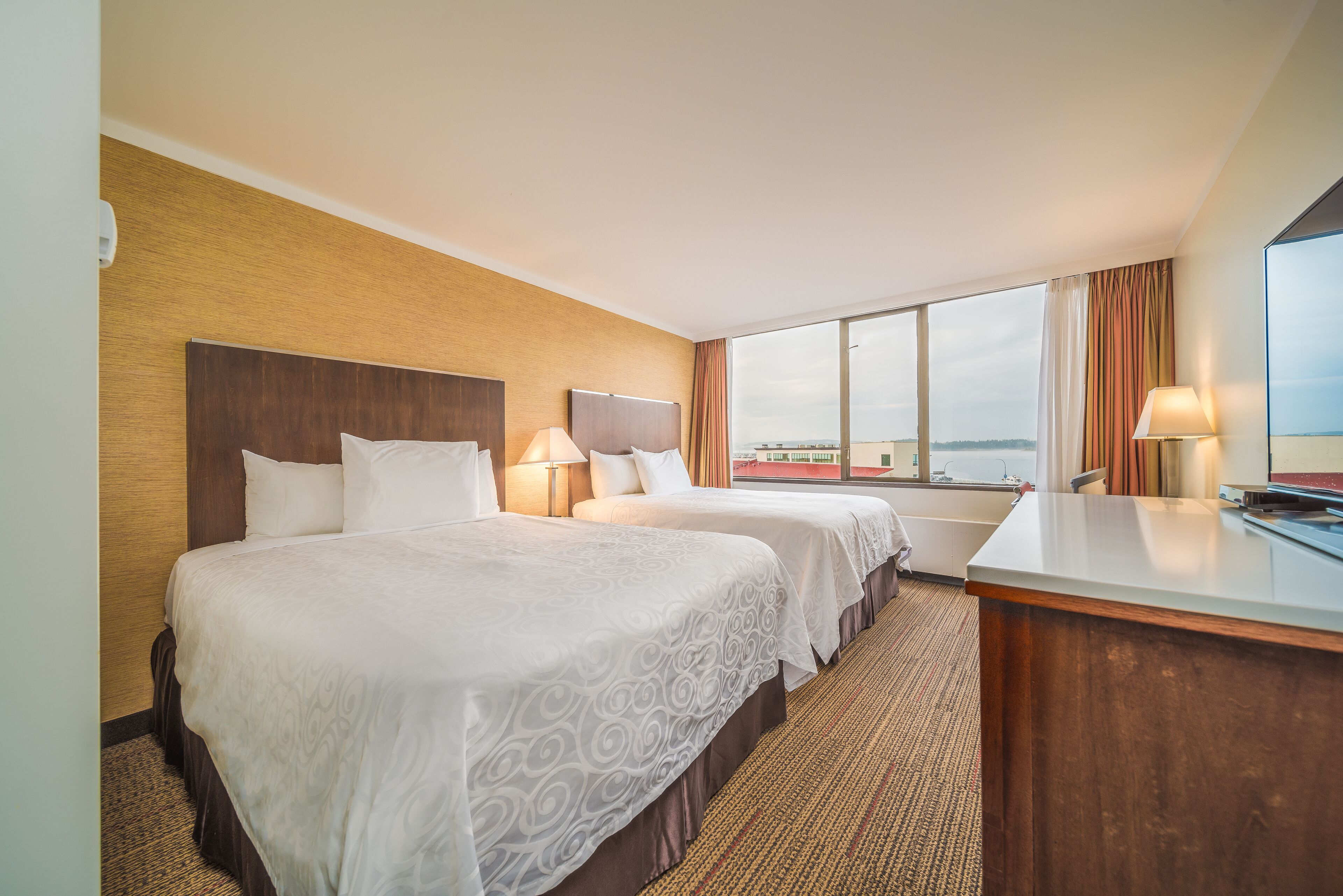 Une chambre d’hôtel avec deux lits, un bureau et une grande fenêtre donnant sur le paysage urbain.
