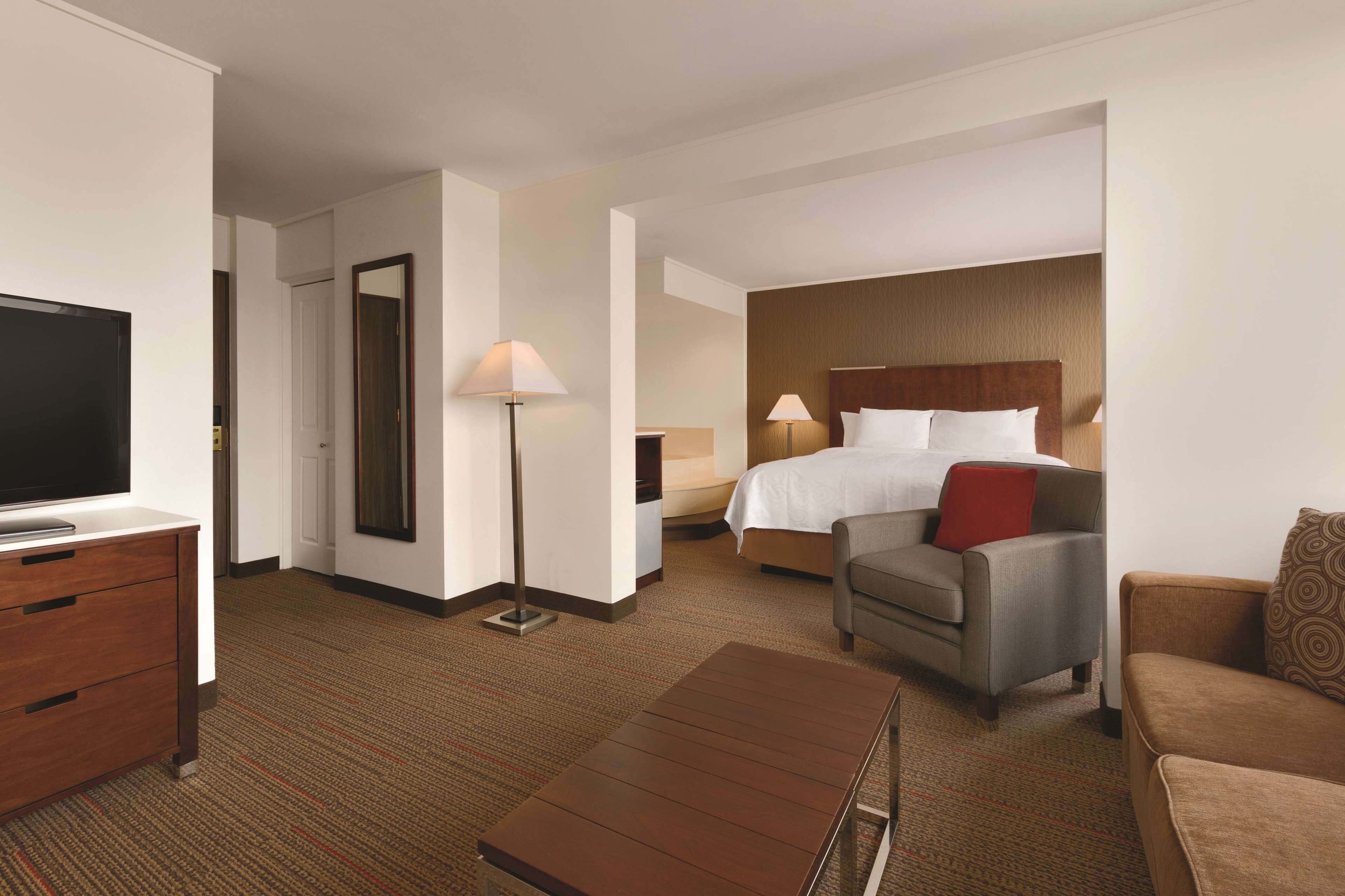 A hotel room with a TV, a desk, a sofa, a bed, and a lamp.