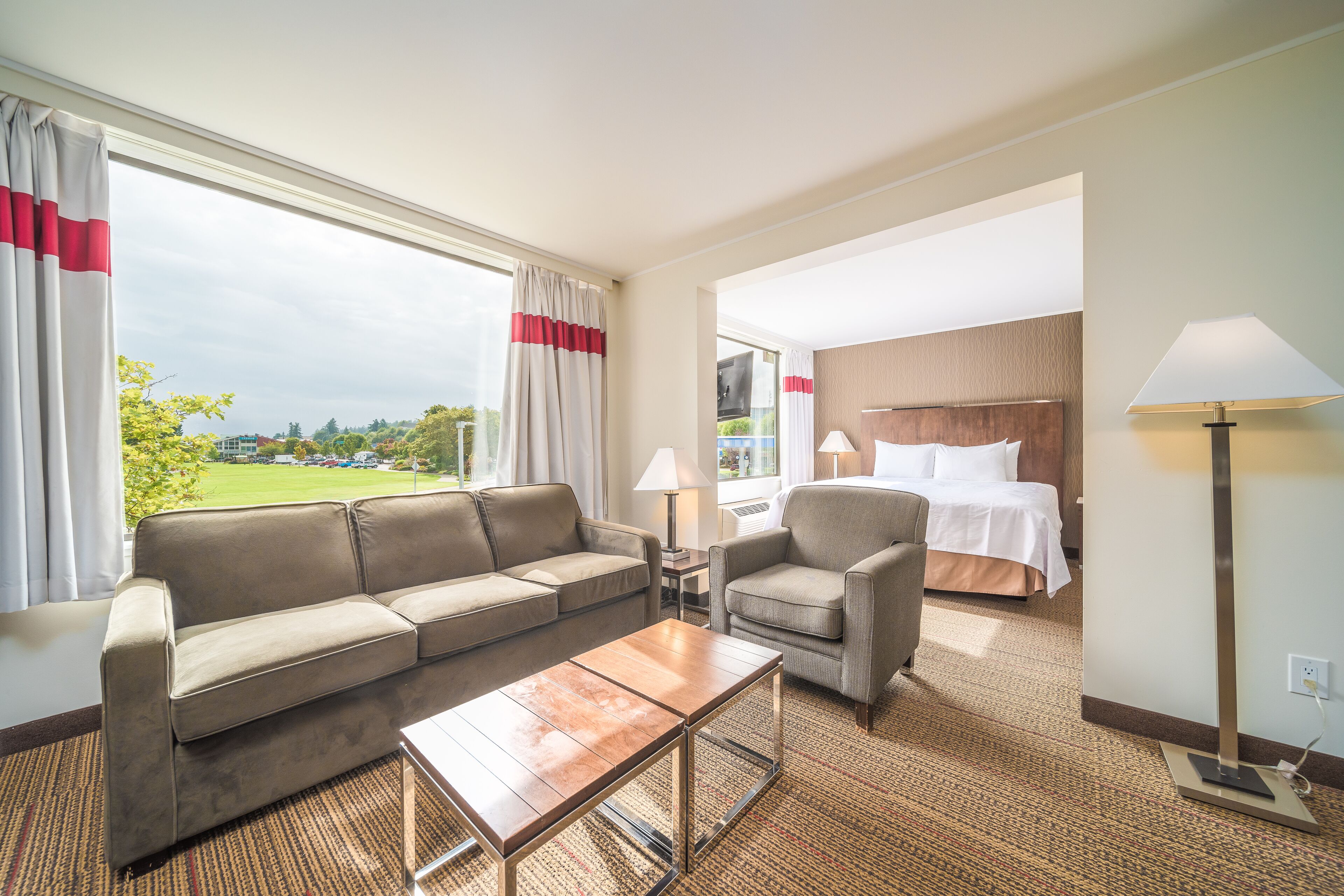 Habitación de hotel con sofá, sillón, cama y vistas al exterior.